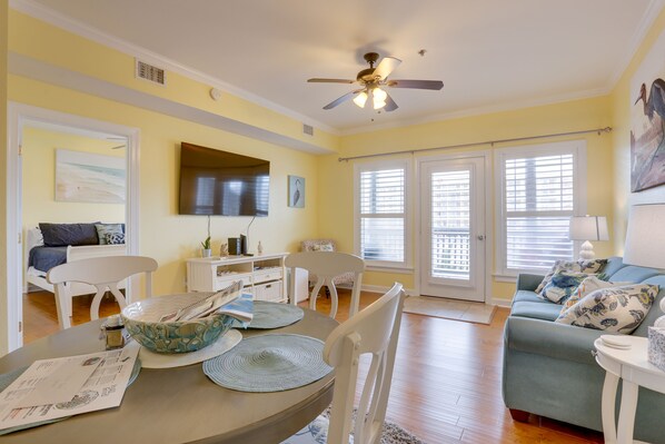 A bright living room with a dining table, chairs, a sofa, and a ceiling fan.