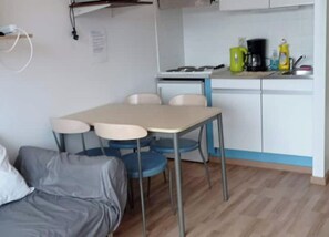 Et kompakt værelse med tekøkken, spisebord med fire stole og en sofa.