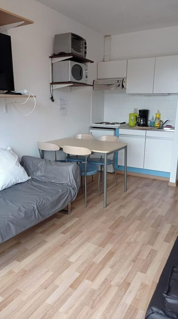 En kompakt opholdsstue med et tekøkken, spiseplads og sofa.