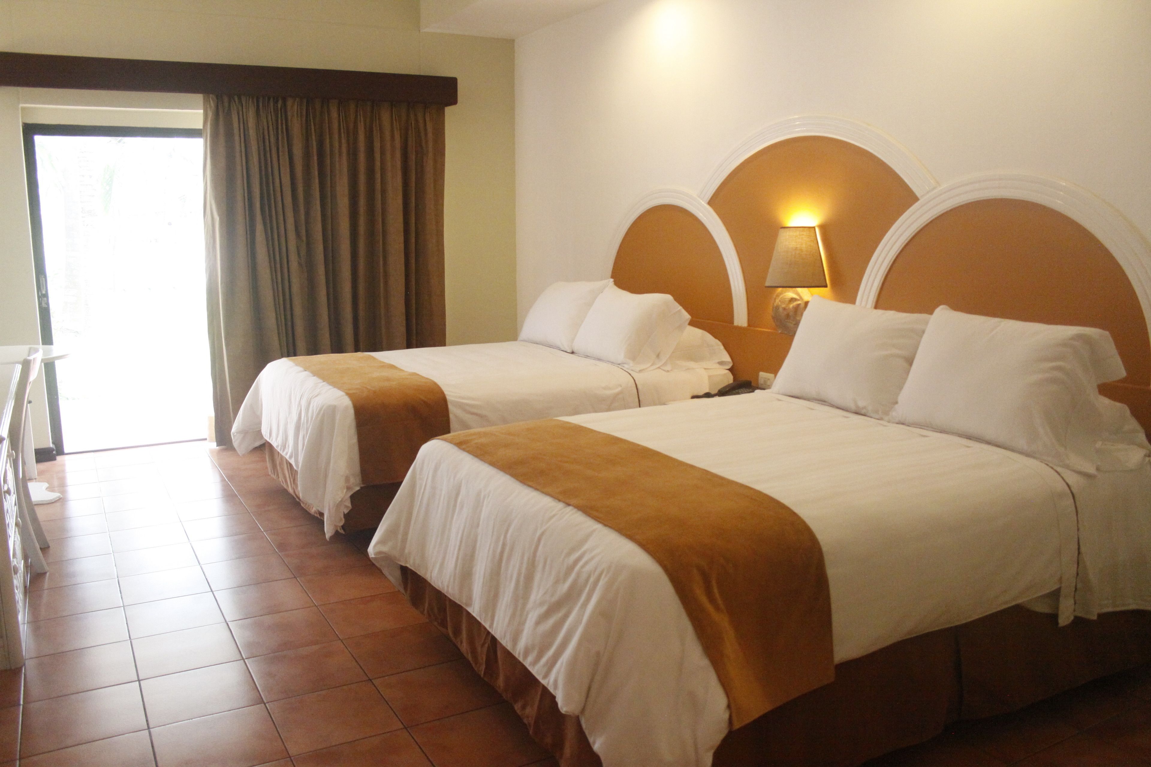 Habitación de hotel con dos camas, un rincón de descanso y un gran ventanal con cortinas.