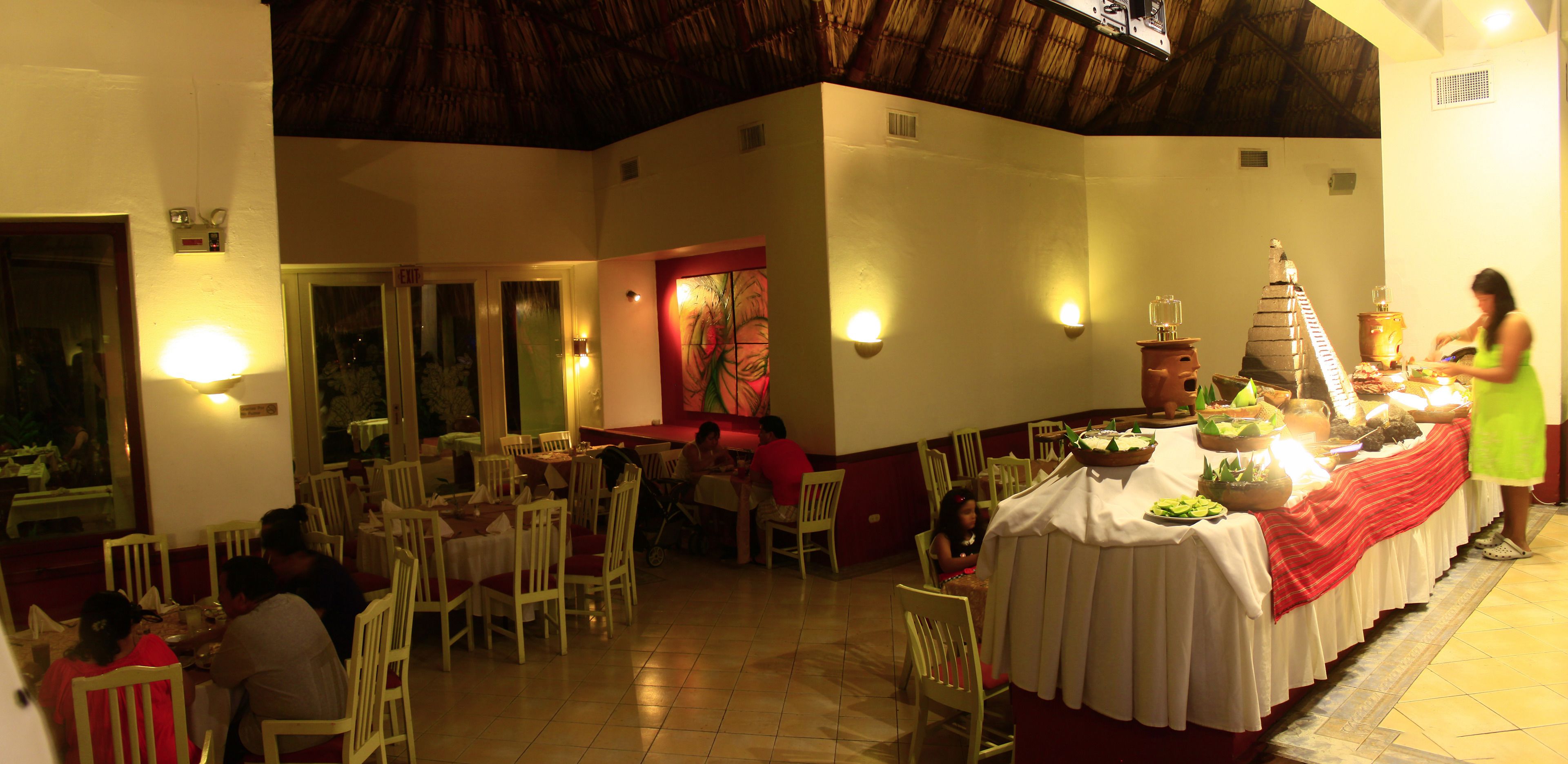 Un restaurante con varias mesas y sillas, una barra de buffet y una persona sirviendo comida.