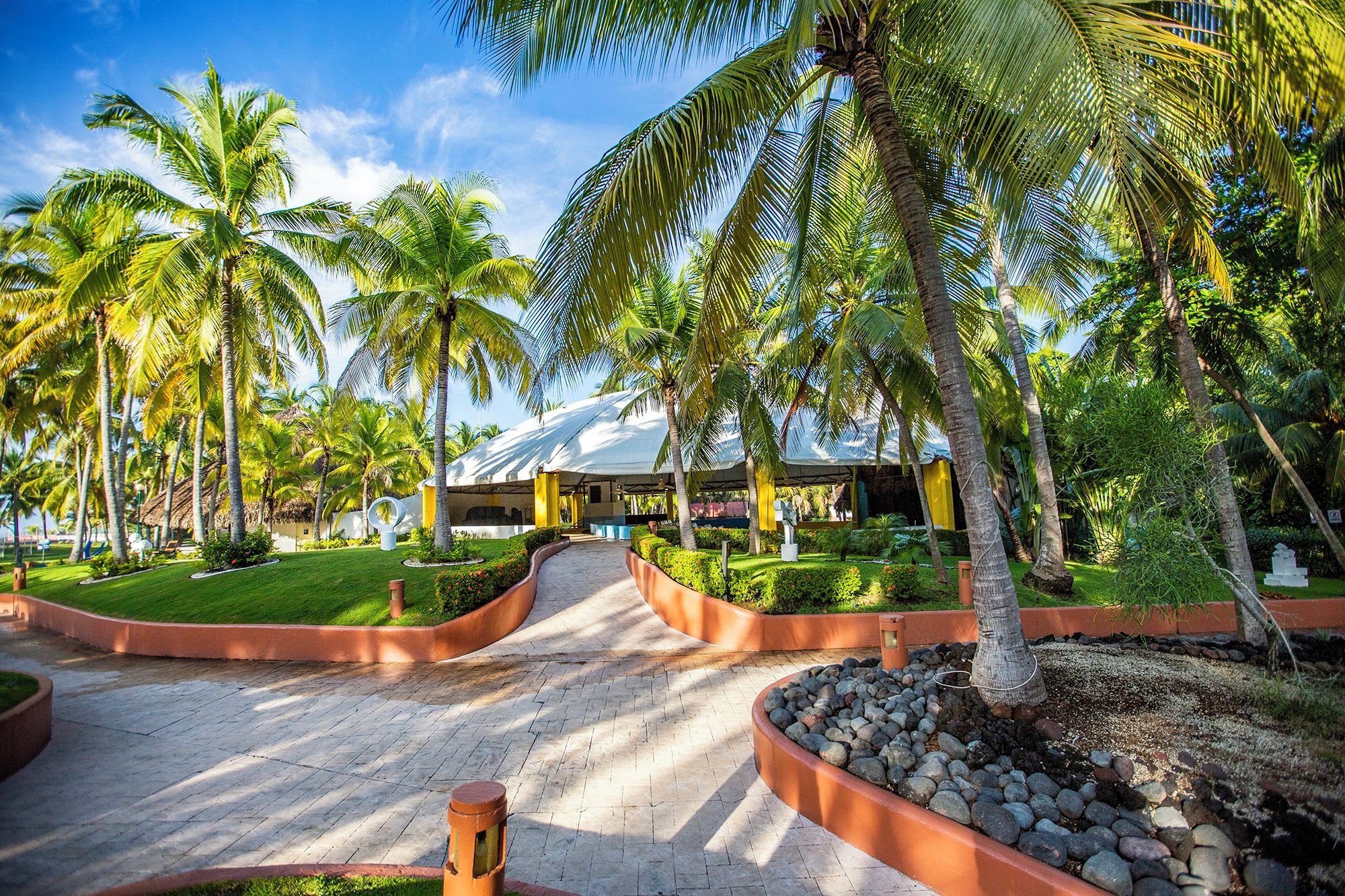 Un resort tropical con palmeras, un paseo techado y un edificio con estructura en forma de cúpula.