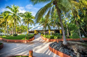 Un resort tropical con palmeras, un paseo techado y un edificio con estructura en forma de cúpula.