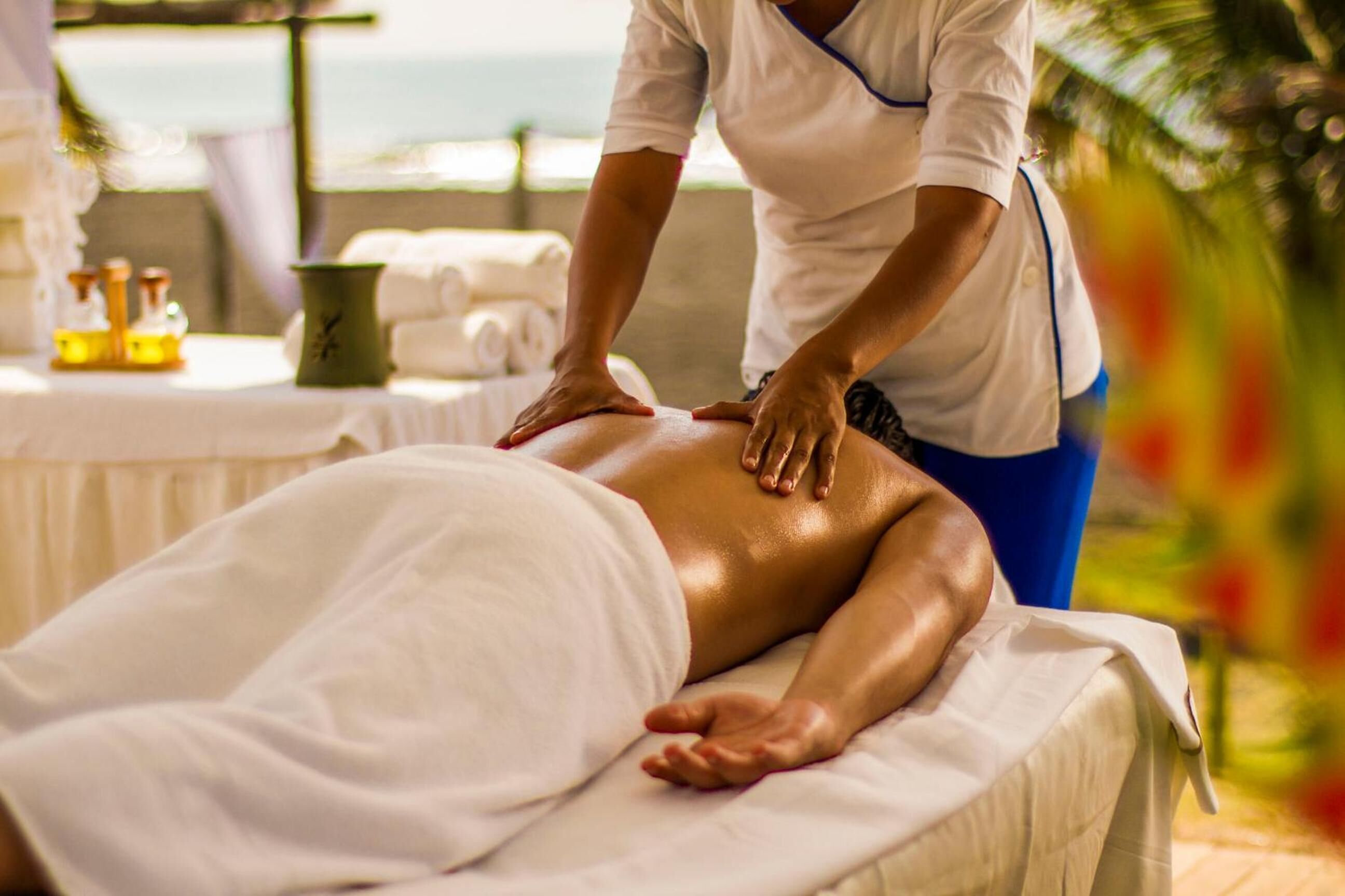 A massage therapy session in a room with a view of the sea, a table with towels, and a small plant.