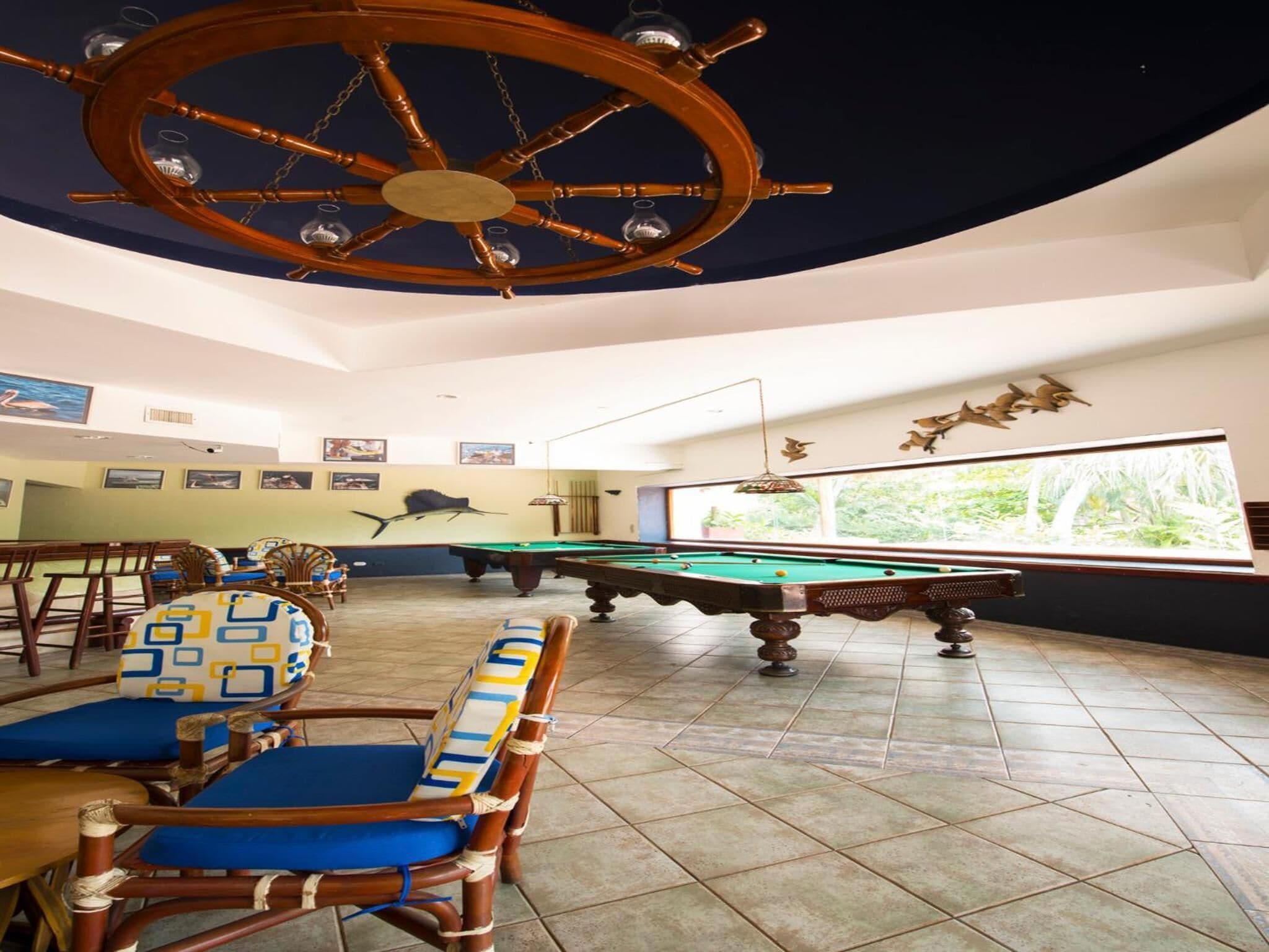 A pool area with a pool table, chairs, and a large wooden ship wheel.