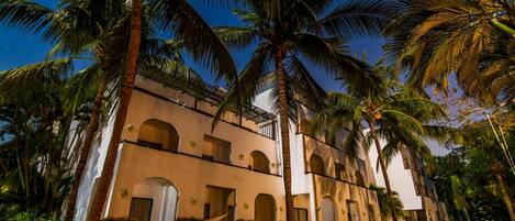 A multi-story building with arched windows and balconies, surrounded by palm trees and well-maintained lawns.