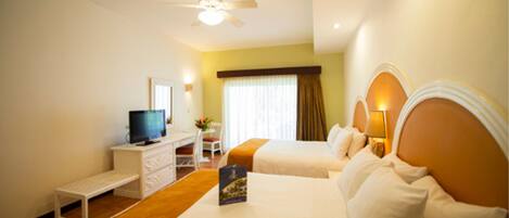 Habitación de hotel con dos camas, un escritorio con televisor, ventilador de techo y ventana con cortinas.