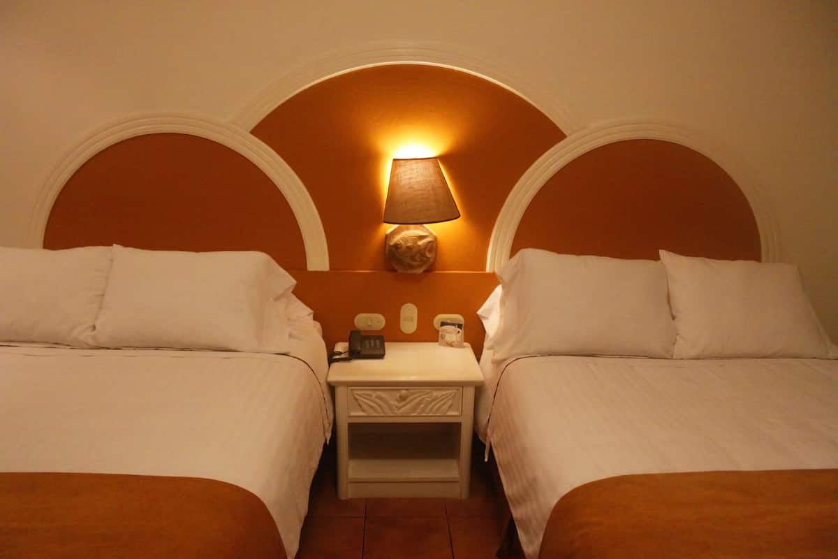Una habitación de hotel con dos camas, una mesita de noche, una lámpara y un teléfono en la pared.