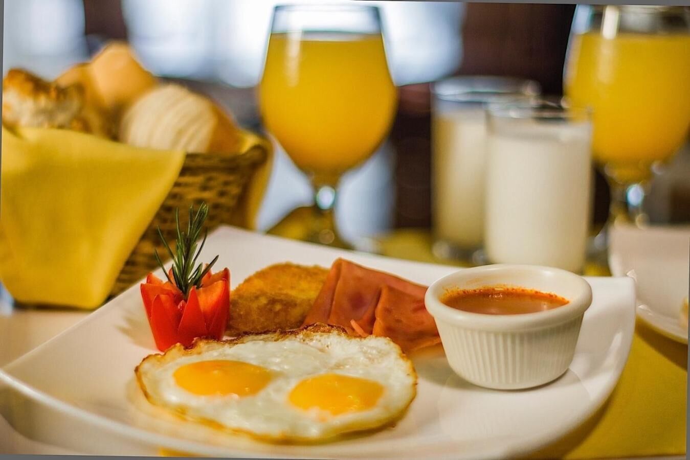 Une assiette de petit-déjeuner comprenant des œufs, du jambon et une petite portion de sauce, accompagnée de croissants et de jus d’orange.
