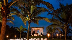 A tropical outdoor wedding setup with a canopy and white draped chairs.