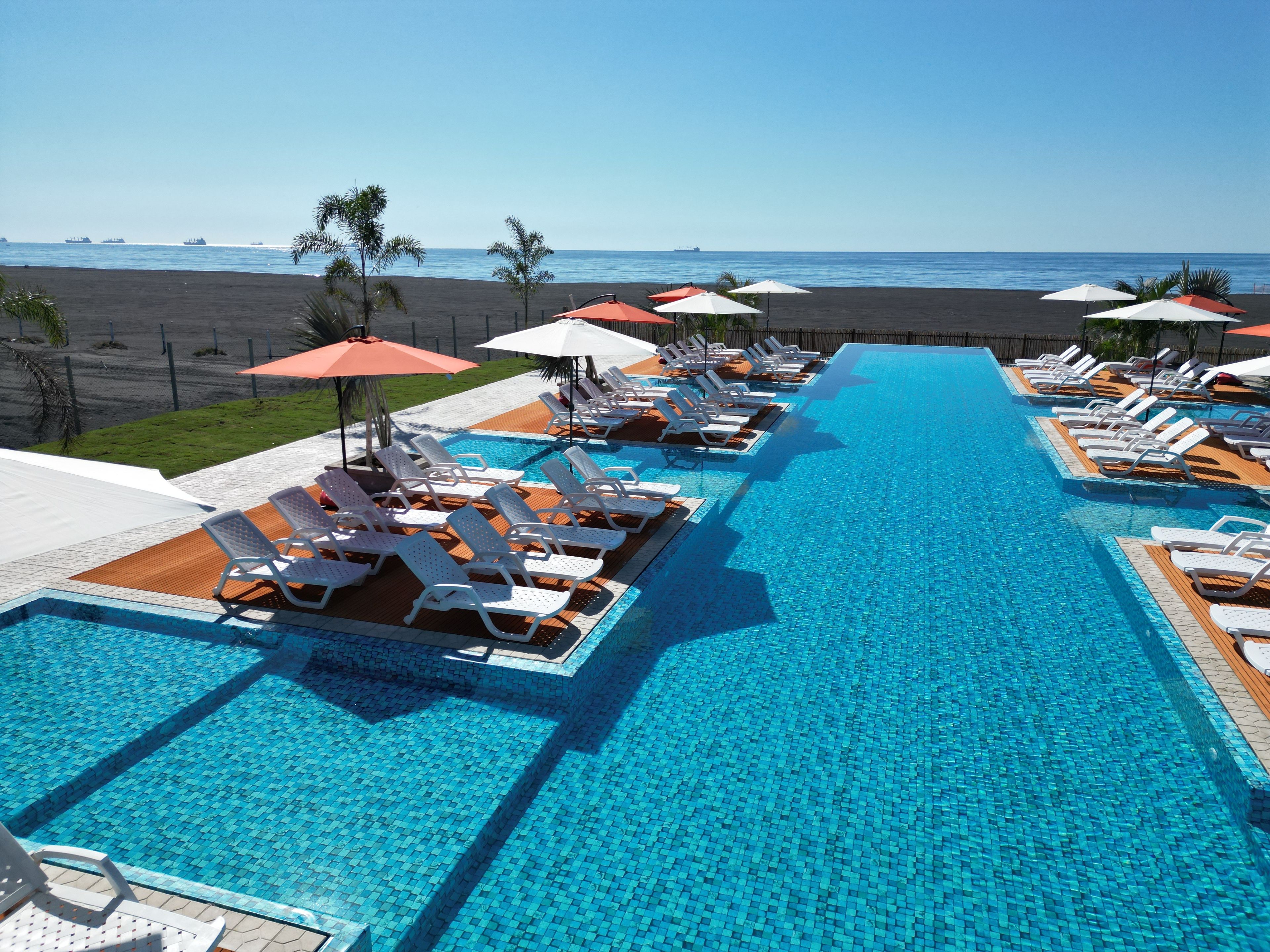 A poolside area with lounge chairs and umbrellas, a clear view of the beach, and a calm sea.