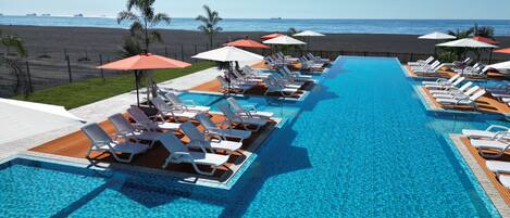 A poolside area with lounge chairs and umbrellas, a clear view of the beach, and a calm sea.