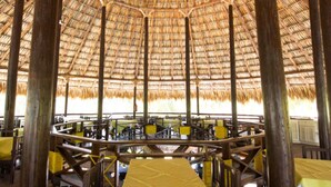 A circular dining area with thatched roof and wooden pillars. Tables are arranged around the perimeter, and chairs are placed in the center.