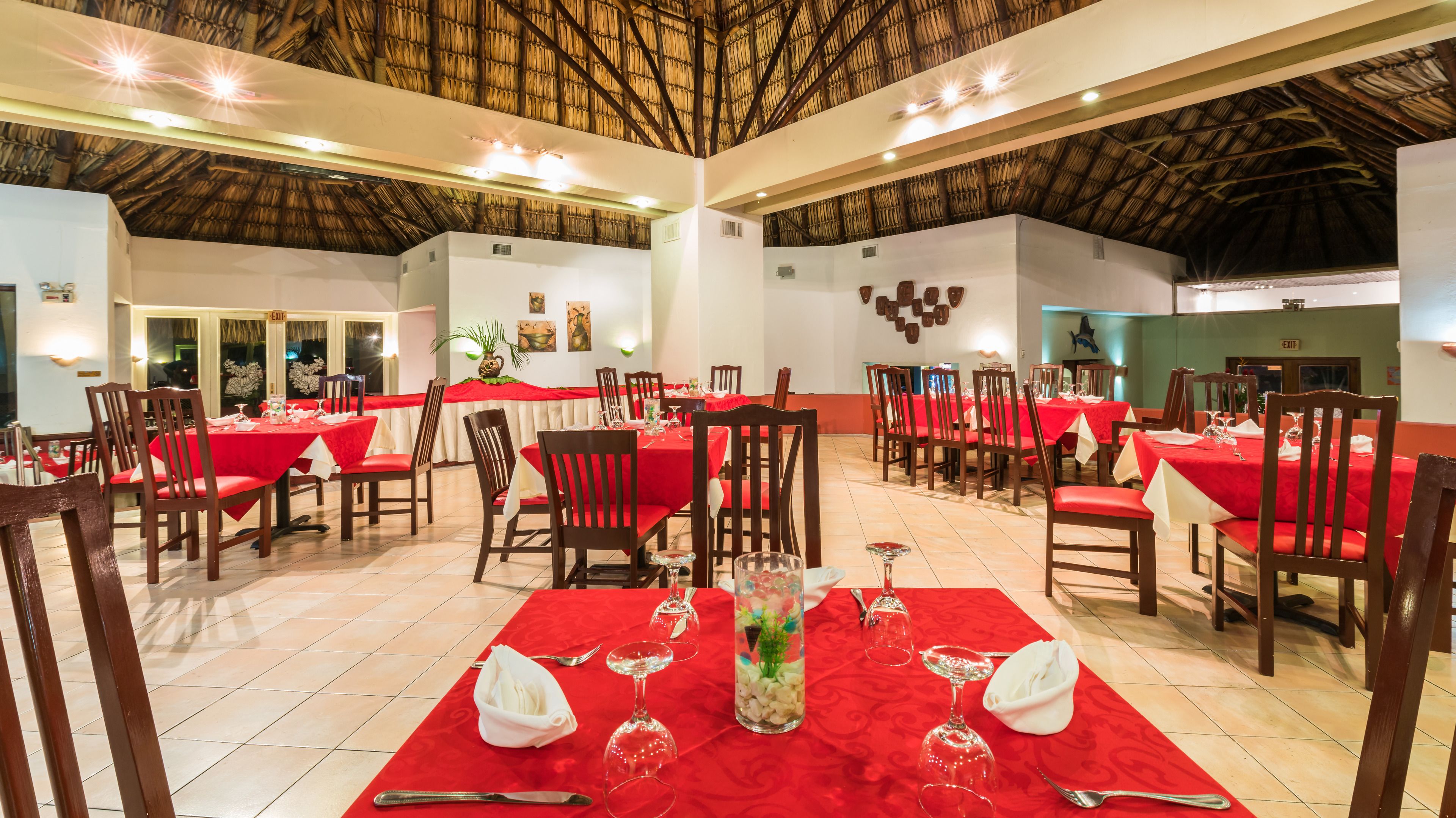 A restaurant with multiple tables set for dining, featuring red tablecloths and wooden chairs.