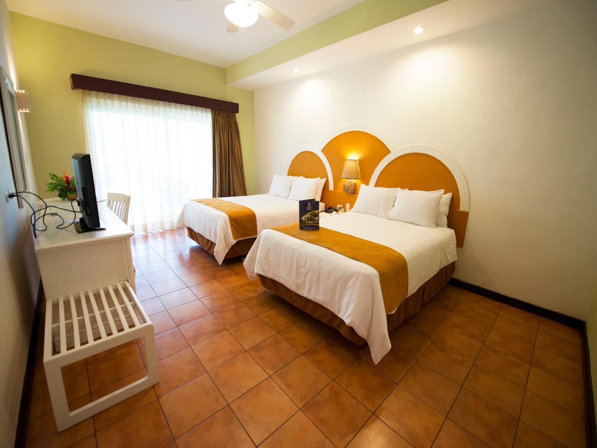 Habitación de hotel con dos camas, un escritorio con computadora y una ventana con cortinas.