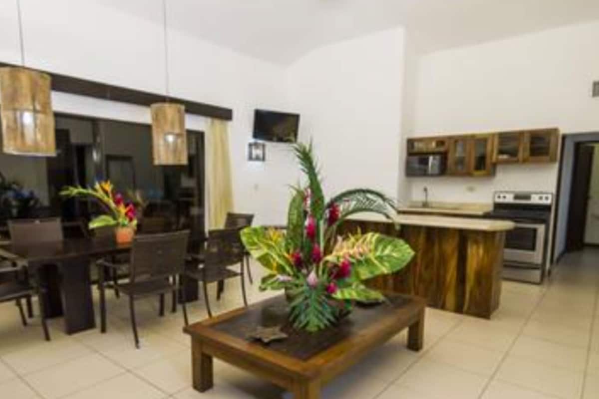 Una sala de estar moderna con una mesa de centro de madera, comedor con sillas y una cocina con mostrador y electrodomésticos.