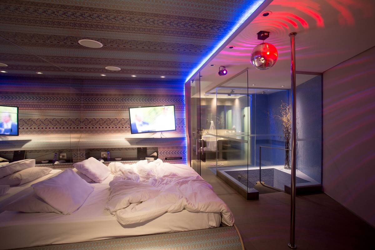 Una habitación de hotel moderna con una cama grande, un televisor y un baño con paredes de vidrio.