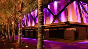 A building with a modern design, featuring a series of illuminated panels and palm trees in the foreground. - Lush Motel Ipiranga (São Paulo)