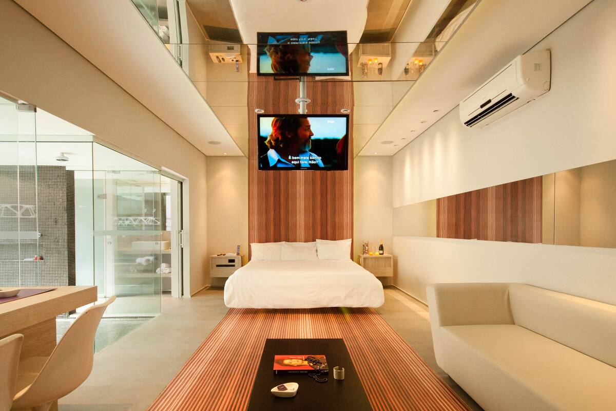 Una habitación de hotel moderna con una cama, un sofá, un escritorio y dos televisores instalados en la pared.
