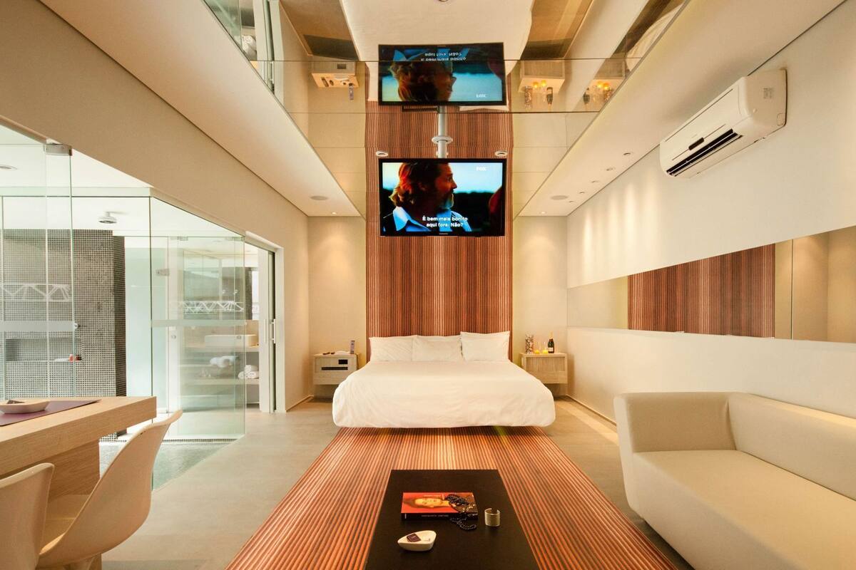 Una habitación de hotel moderna con una cama, un televisor montado en la pared, un escritorio y una zona de estar.