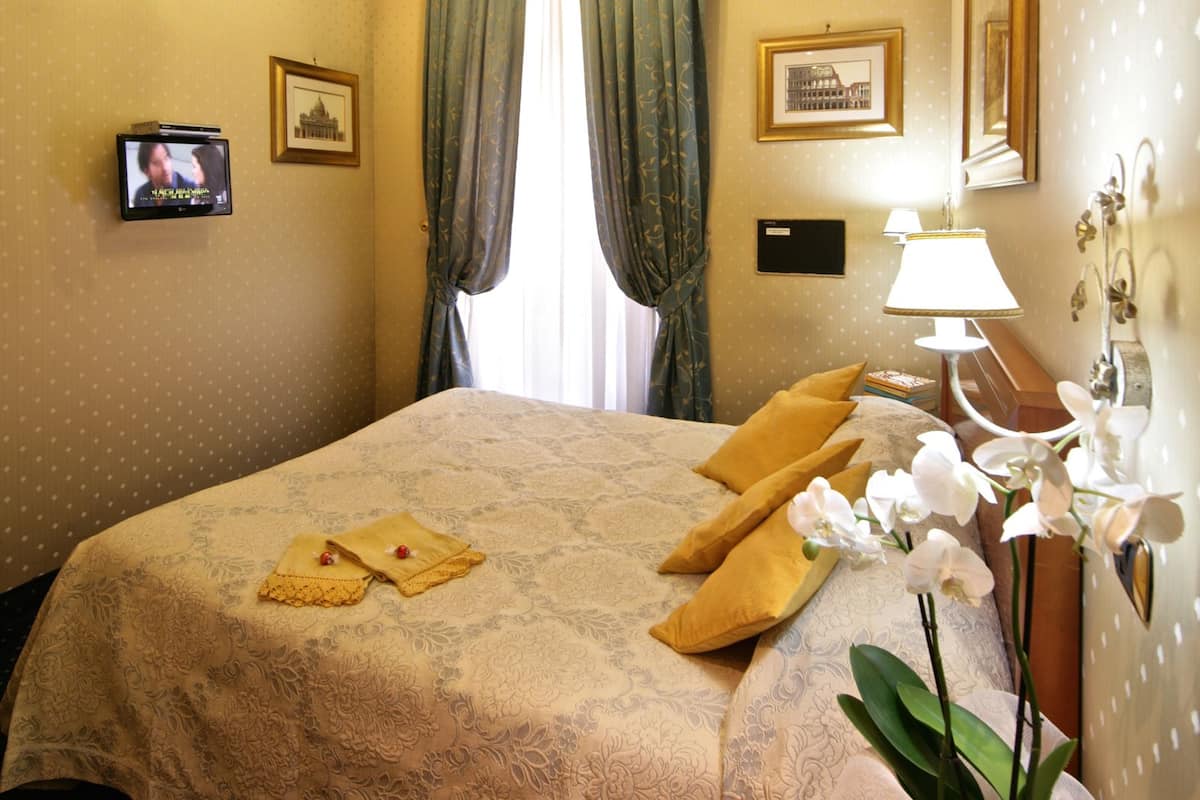 A hotel room with a bed, a television, a lamp, and a vase with flowers.