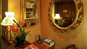 A hotel reception desk with a lamp, a framed painting, a mirror, a telephone, and a chair. - Vatican Holiday (Rome)