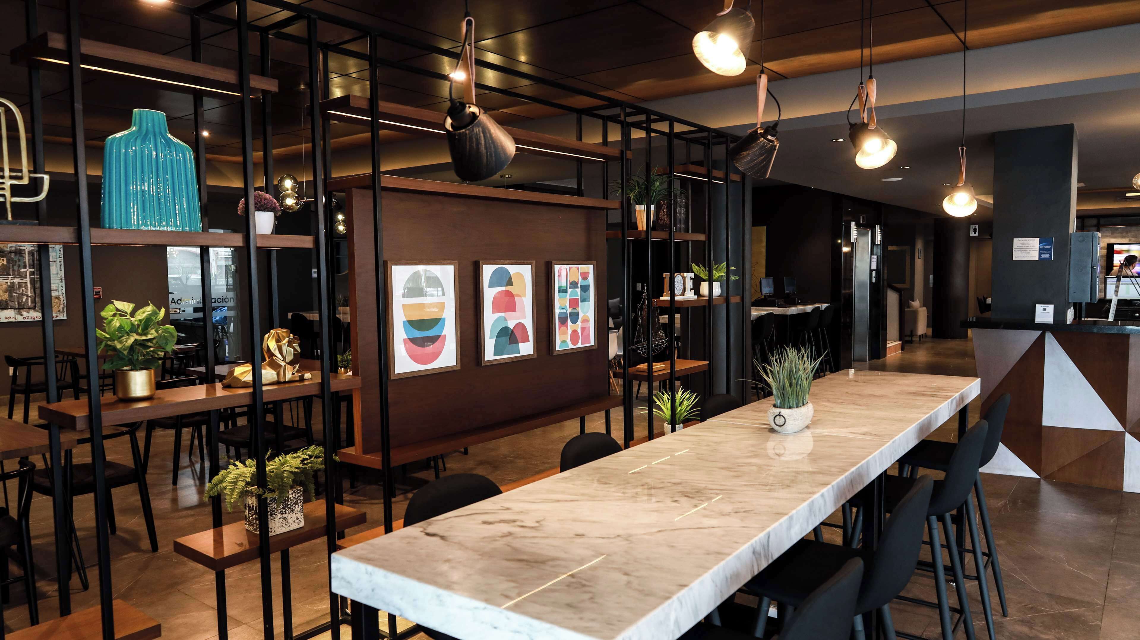 A modern interior with a long marble counter, wooden tables, black chairs, and hanging pendant lights.