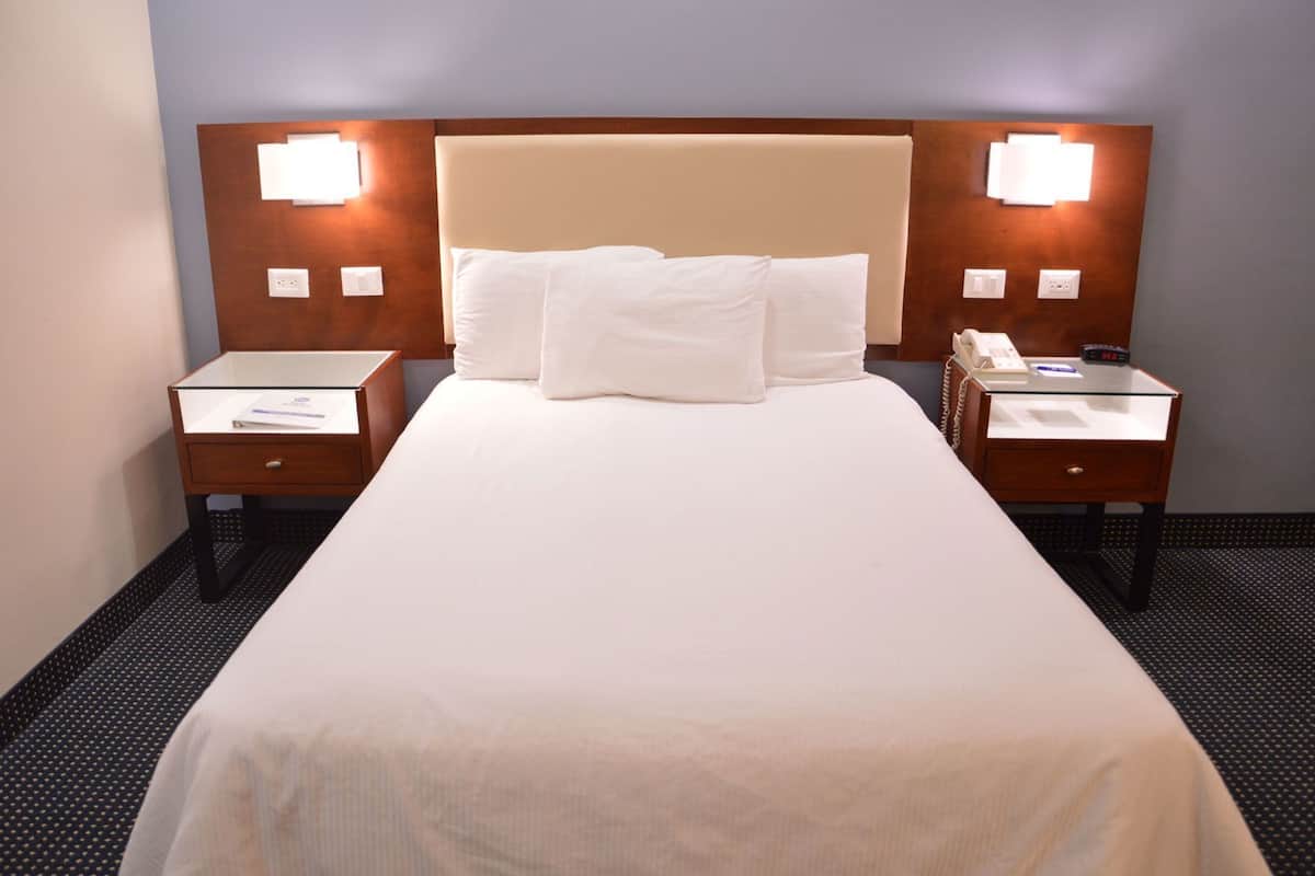 Habitació d'hotel amb un llit gran, dues taules de nit i un taulell amb un telèfon, i làmpades penjades a la paret.