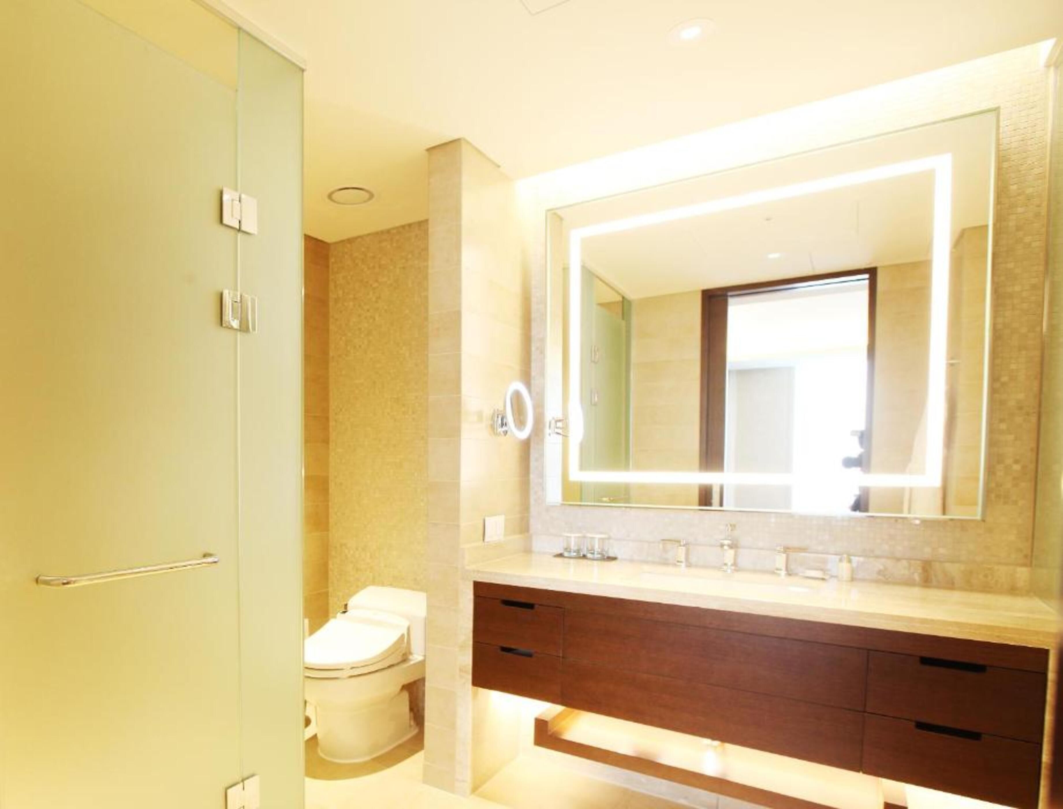 A modern bathroom with a large mirror, a toilet, and a vanity with drawers.