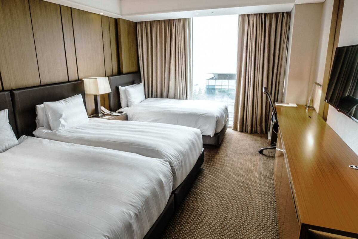 A hotel room with two beds, a wooden headboard, a desk, and a TV.