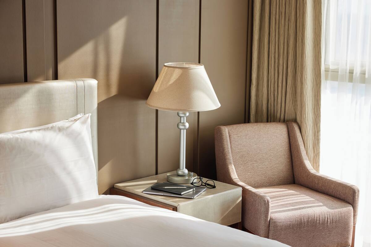 A hotel room with a bed, a nightstand with a lamp, a chair, and a window with curtains.