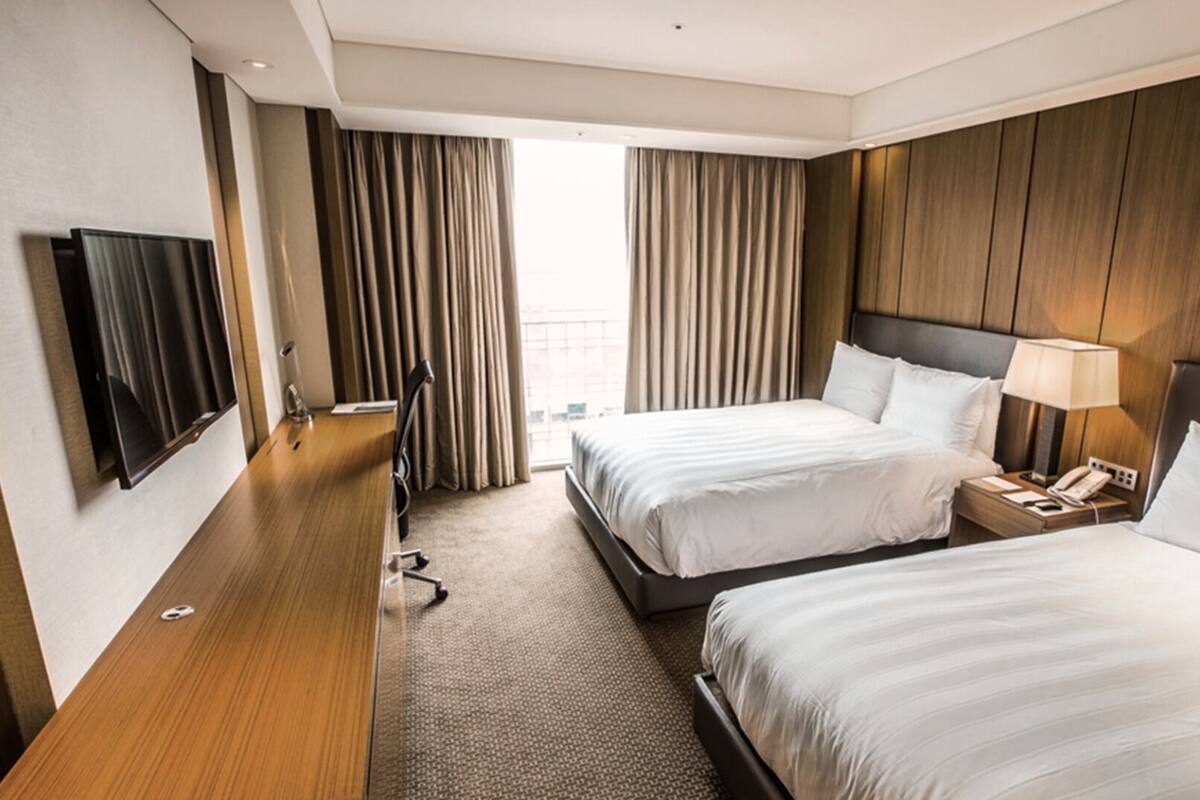 A hotel room with two beds, a desk with a chair, a TV, and a window with curtains.