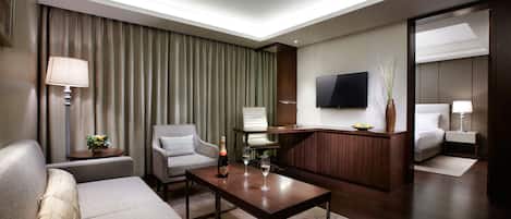 A hotel room with a sofa, armchair, coffee table, and a TV mounted on the wall.
