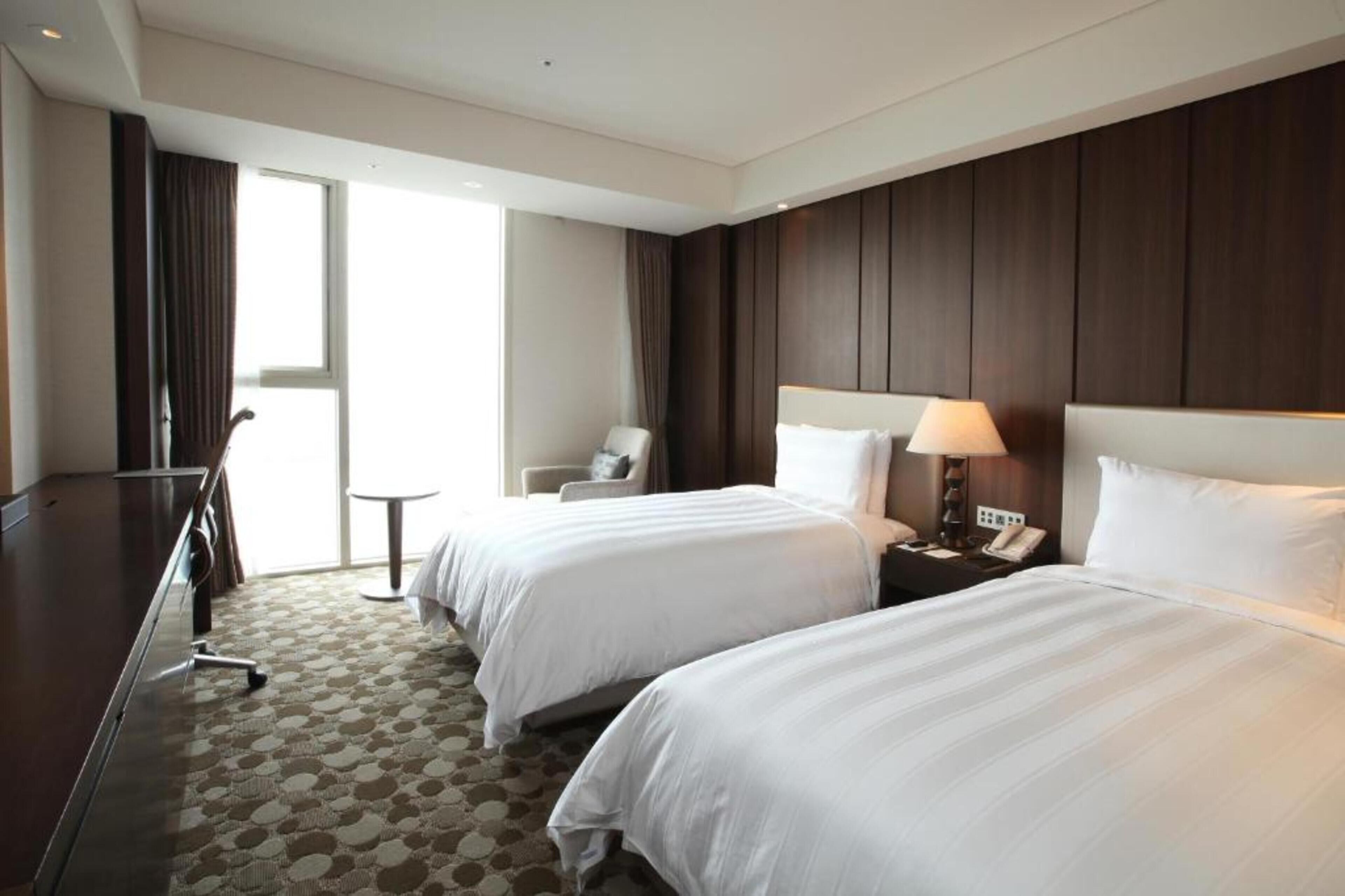 A hotel room with two beds, a desk, a chair, a small table, and a window with curtains.