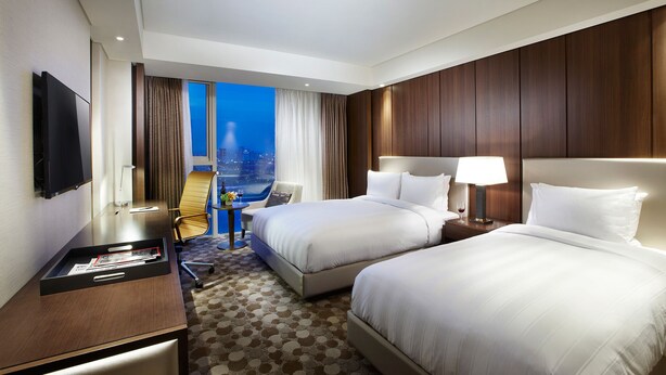 Habitación de hotel con dos camas, un escritorio, un televisor y vista a la ciudad de noche.