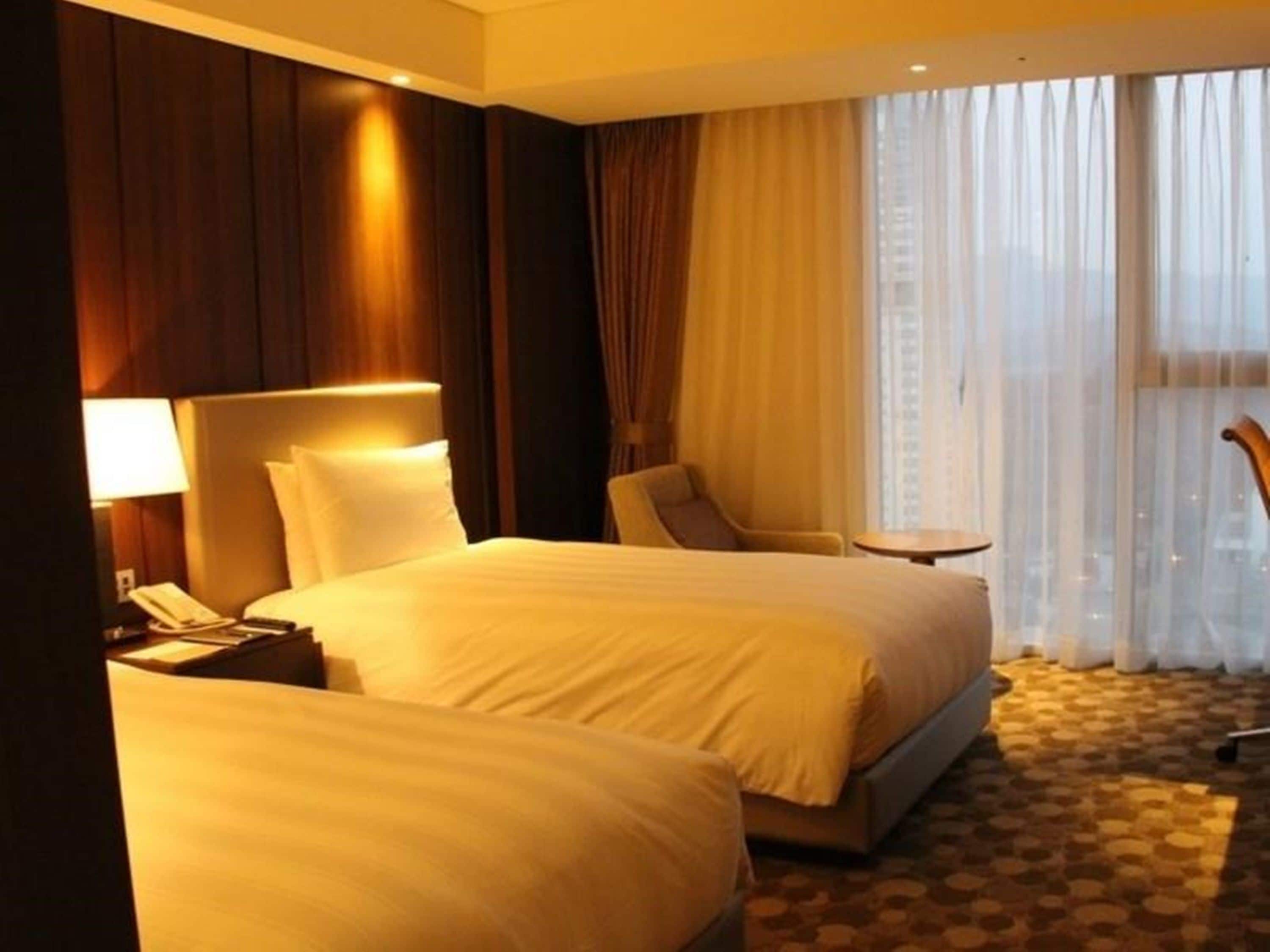 A hotel room with two beds, a desk, a chair, and a window with curtains.