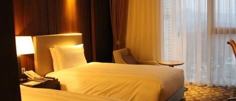 Una habitación de hotel con dos camas, un escritorio, una silla y una ventana con cortinas.