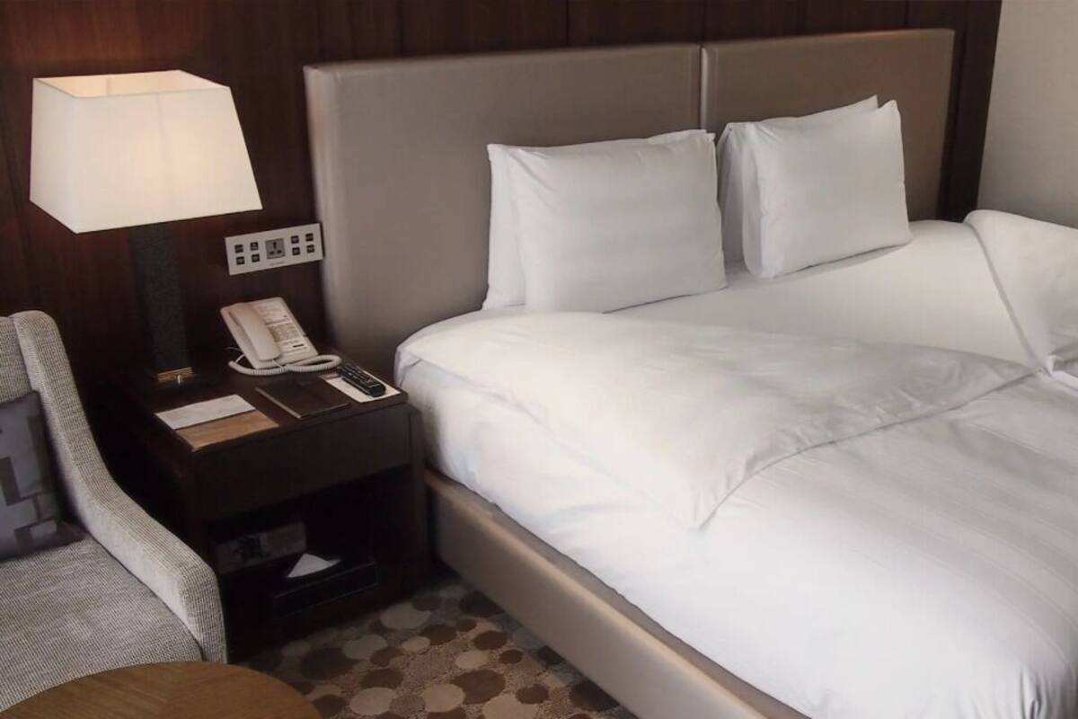 A hotel room with a bed, a nightstand with a lamp, a telephone, and a chair.