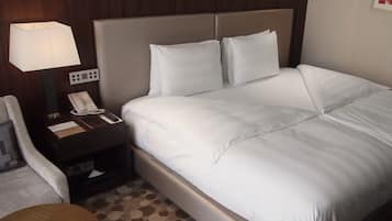 Et hotelværelse med en seng, et natbord med lampe, en telefon og en stol.