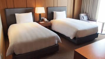A hotel room with two beds, a nightstand with a lamp, a chair, and a wooden headboard.