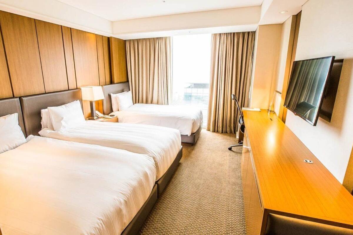 Habitación de hotel con dos camas, un escritorio, un televisor y una ventana con cortinas.