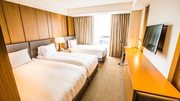 A hotel room with two beds, a desk, a TV, and a view of the outdoors.