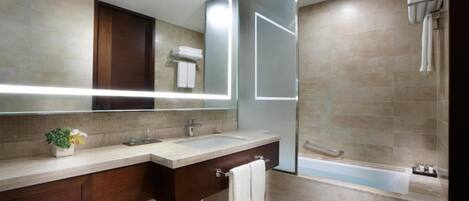 A modern bathroom with a large mirror, two sinks, a vanity, and a bathtub.