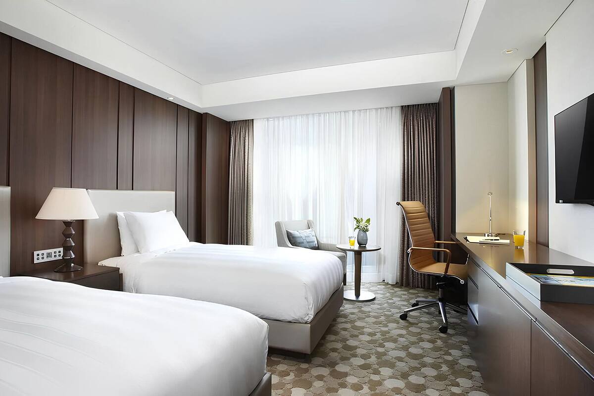 A hotel room with two beds, a desk, a chair, a TV, and a window with curtains.