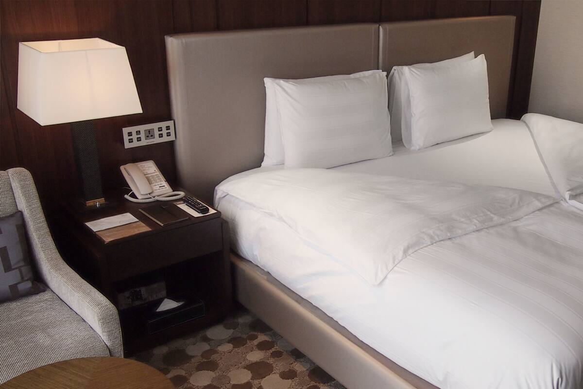 A neatly made bed with white linens, a bedside lamp, a telephone, and a small table with a notepad and pen.