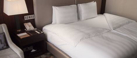 A neatly made bed with white linens, a bedside lamp, a telephone, and a small table with a notepad and pen.