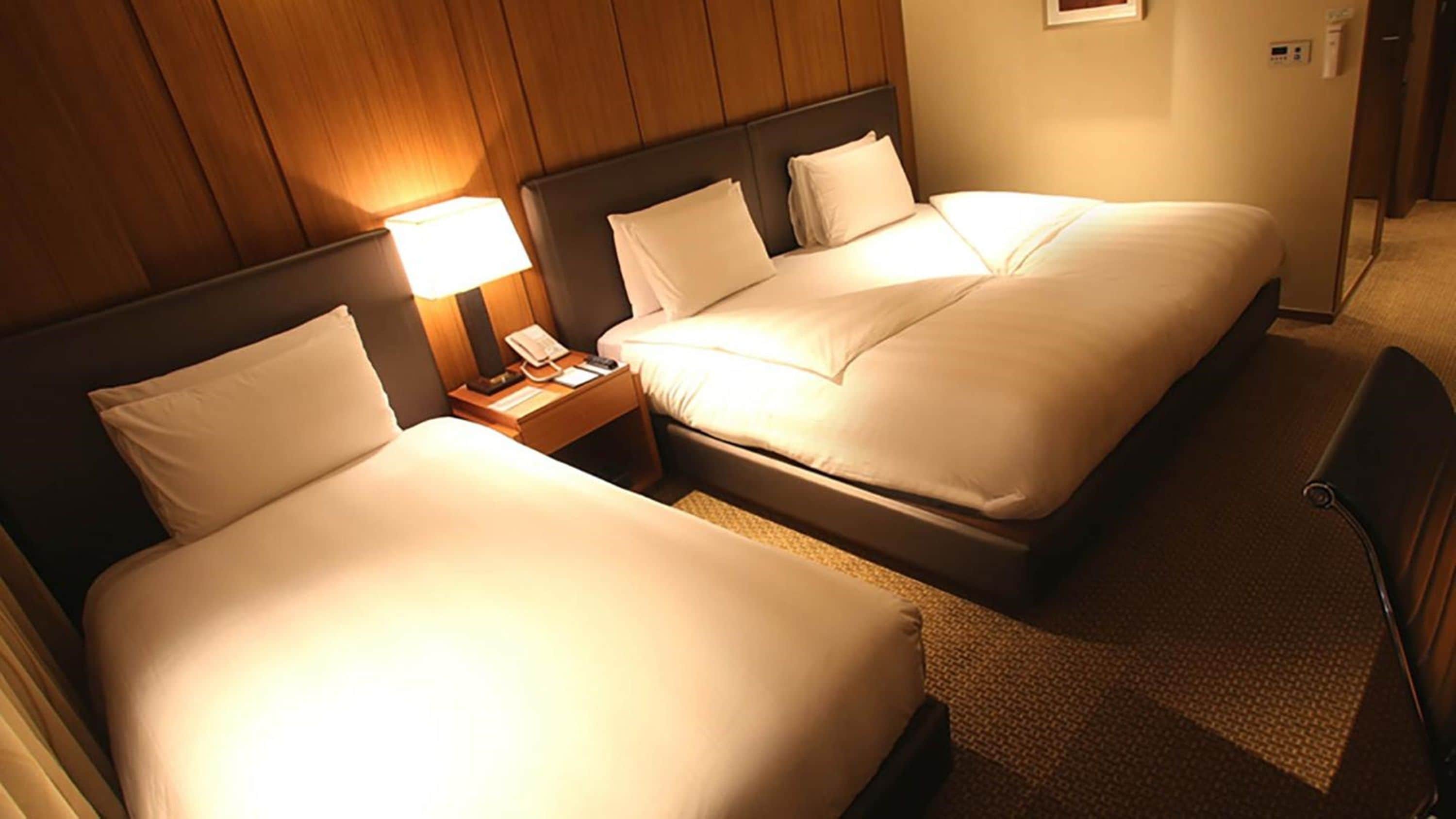 Una habitación de hotel con dos camas, una mesita de noche con lámpara y una silla.