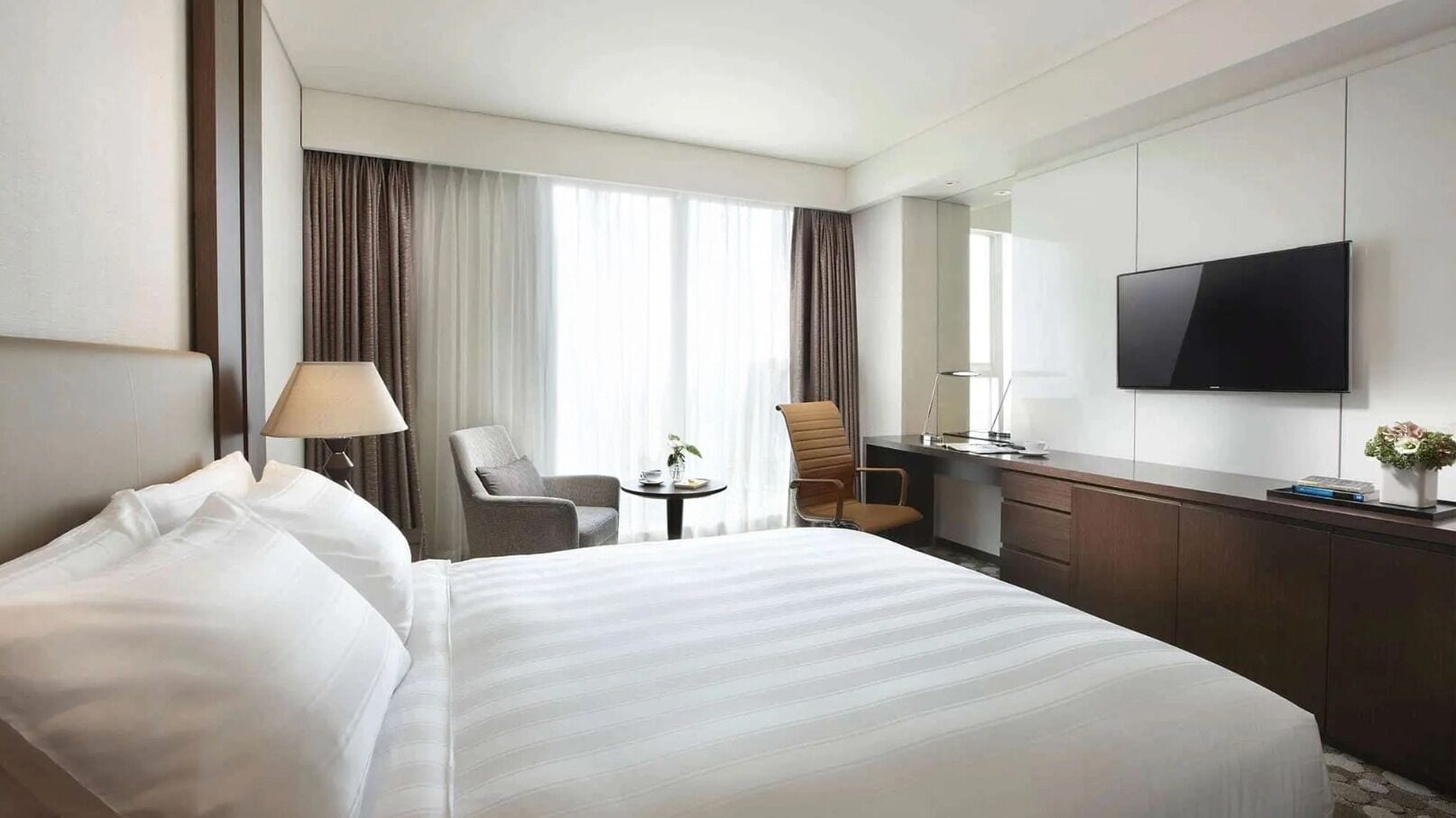 A hotel room with a large bed, a desk, a chair, a TV, and a window with curtains.