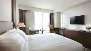 A hotel room with a large bed, a desk, a chair, a TV, and a window with curtains.