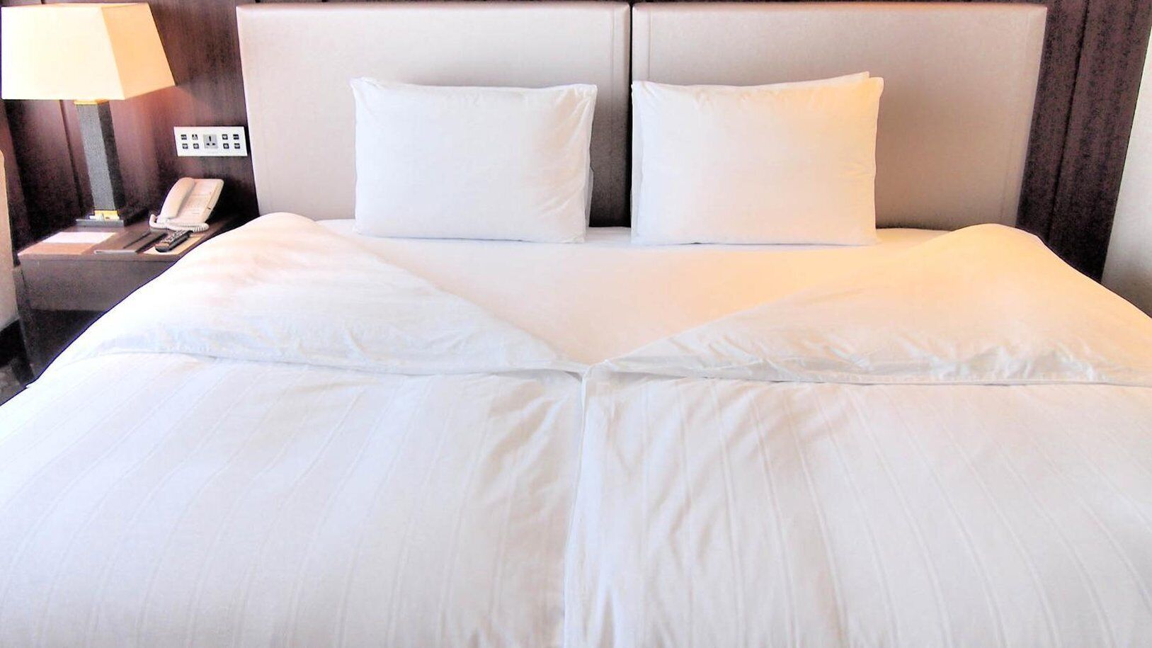 A neatly made bed with white linens, a bedside lamp, and a phone on the nightstand.